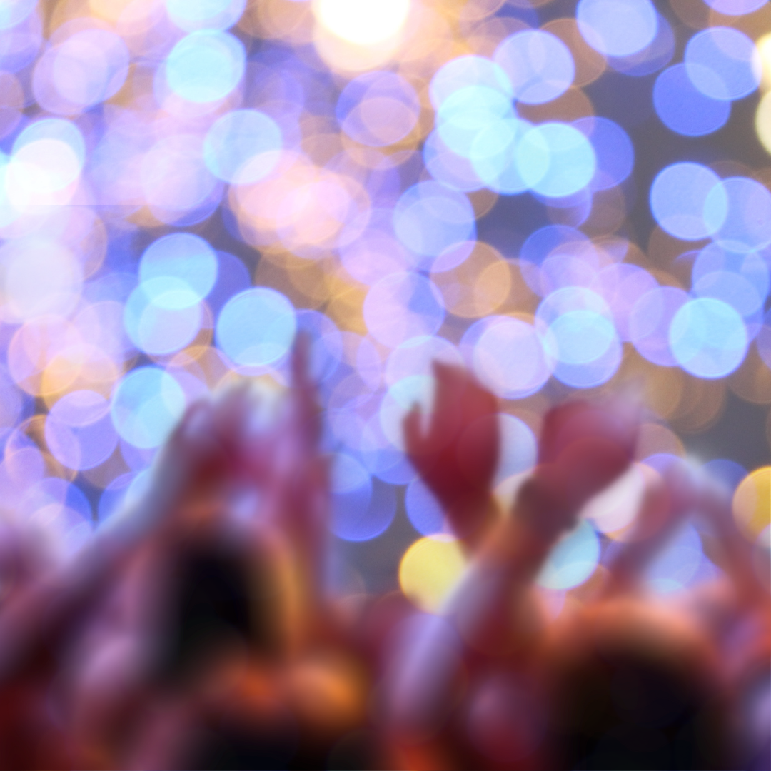 Blurred image of a crowd raising hands with colorful bokeh lights in the background.