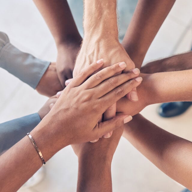 A group of diverse hands stacked together, symbolizing unity and teamwork.