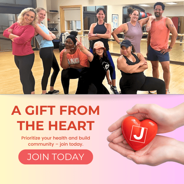 A group of people posing in a gym studio above an image of hands holding a heart with the letter 'J'. Text reads: "A gift from the heart. Join today.